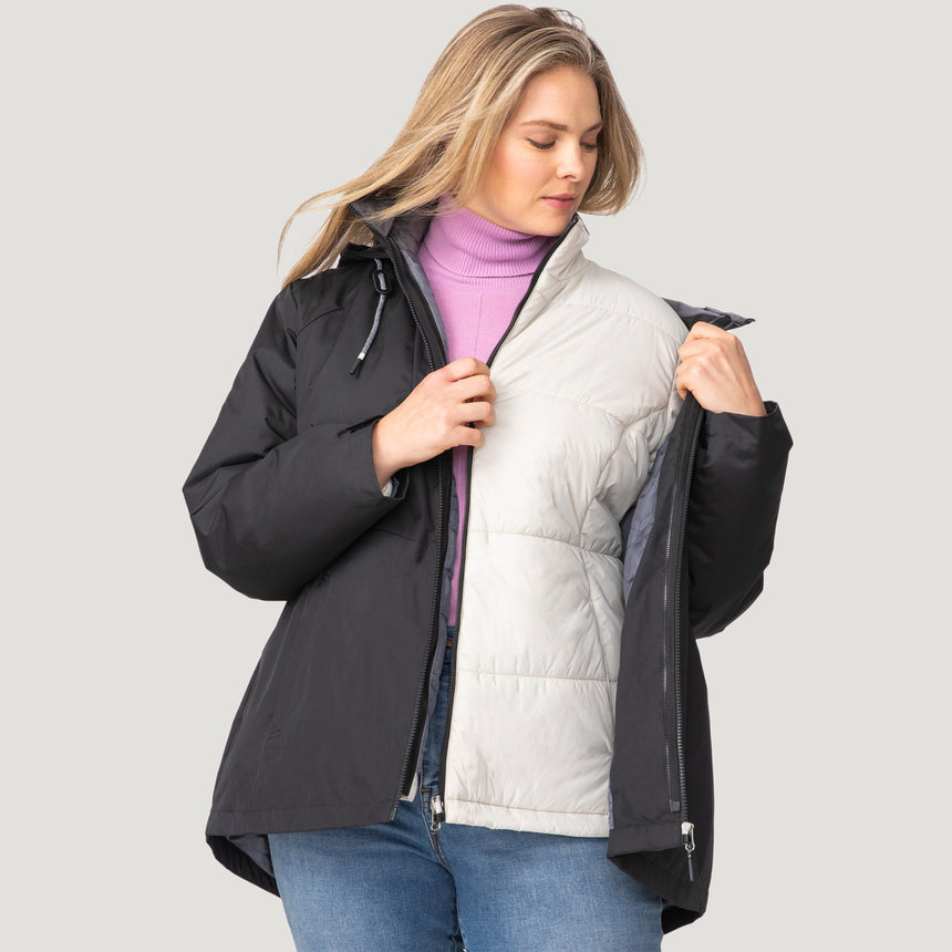 A person wearing the Clearance Women's Plus Size Back of Bell 3-in-1 Systems Jacket in black over a light purple turtleneck and blue jeans unzips the sustainable outerwear to reveal its white inner layer.