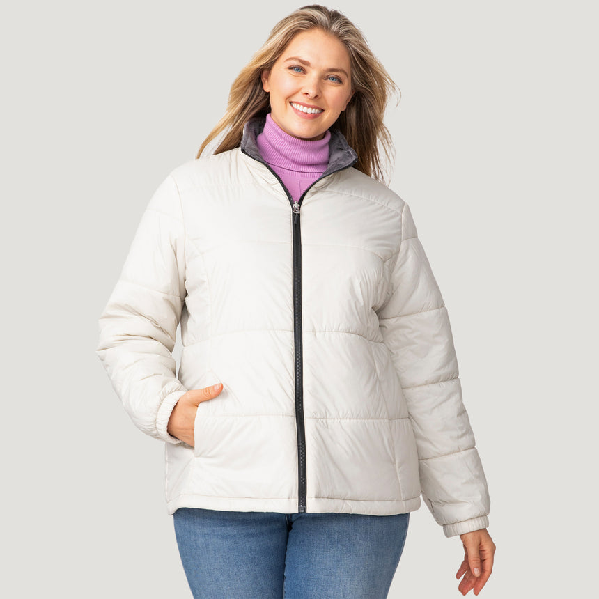 A woman with long blonde hair smiles while wearing the Clearance Women's Plus Size Back of Bell 3-in-1 Systems Jacket over a lavender turtleneck and blue jeans, standing against a plain light gray background.