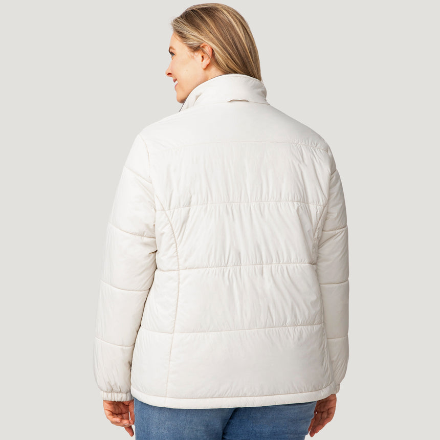A woman with blonde hair, dressed in the Women's Plus Size Back of Bell 3-in-1 Systems Jacket by Clearance—a sustainable white quilted puffer style—pairs it with blue jeans as she stands facing away from the camera against a plain light gray background.