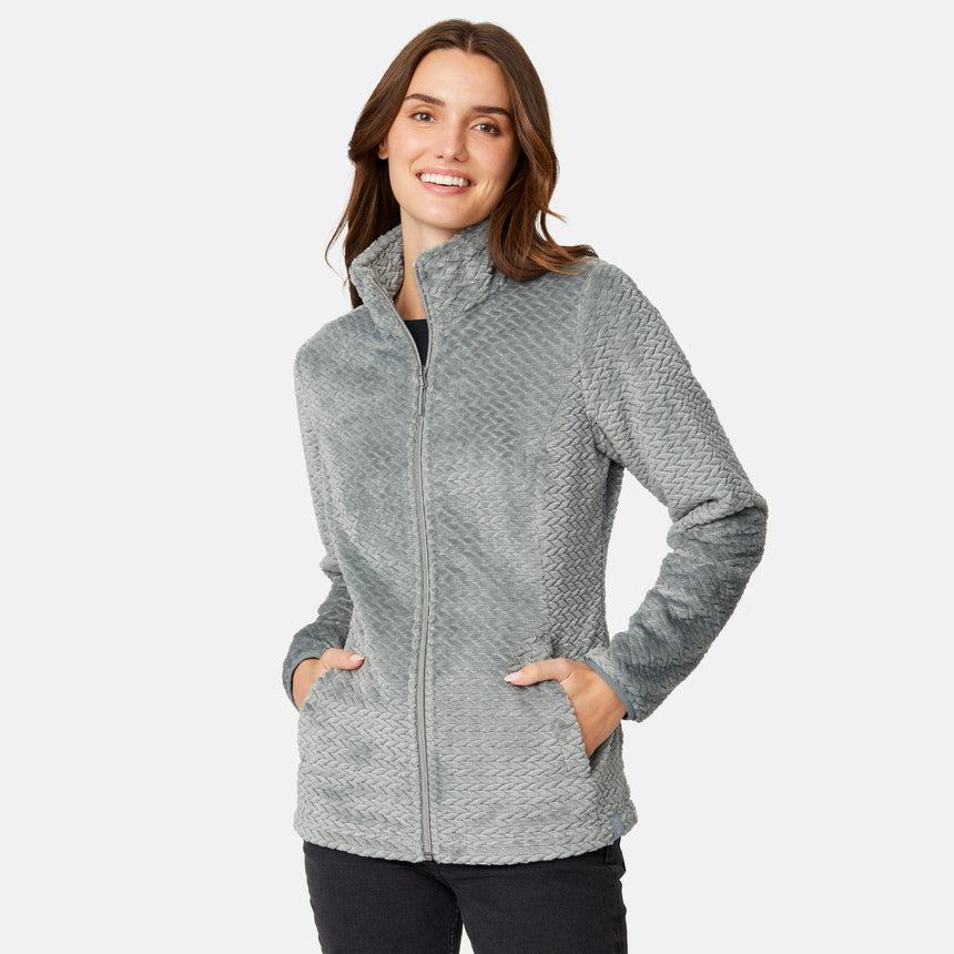 A smiling woman wearing a Cyprus Women’s Cable Braided Butter Pile® Jacket, a super soft, textured cable braided jacket with a grey zip-up front and side pockets.