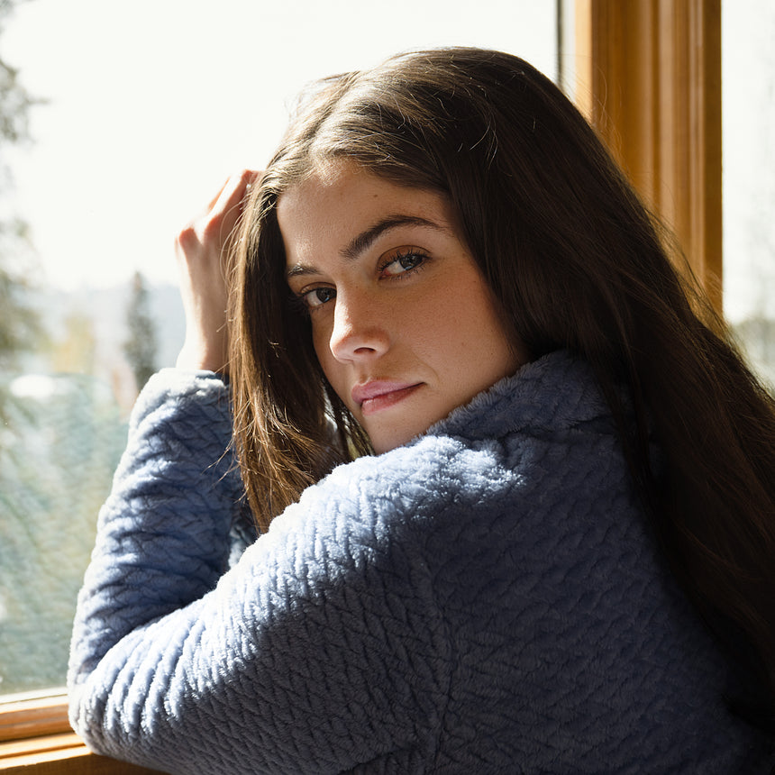 Woman wearing a blue quilted fleece jacket by a window with natural light