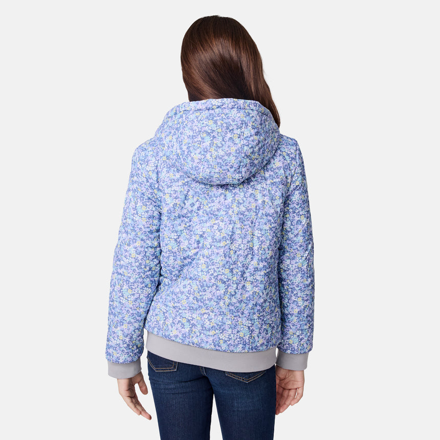 A person is shown from the back against a plain white background, wearing the Clearance Girls' Poofie Reversible Puffer Jacket—a hooded, blue and purple floral recycled polyester jacket—paired with dark jeans.