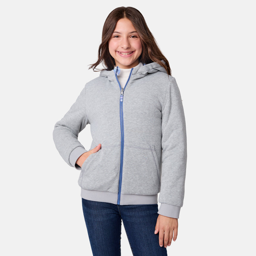 A smiling girl with long brown hair wears the Clearance Girls' Poofie Reversible Puffer Jacket in light gray and blue jeans, standing against a plain white background with one hand in her pocket.