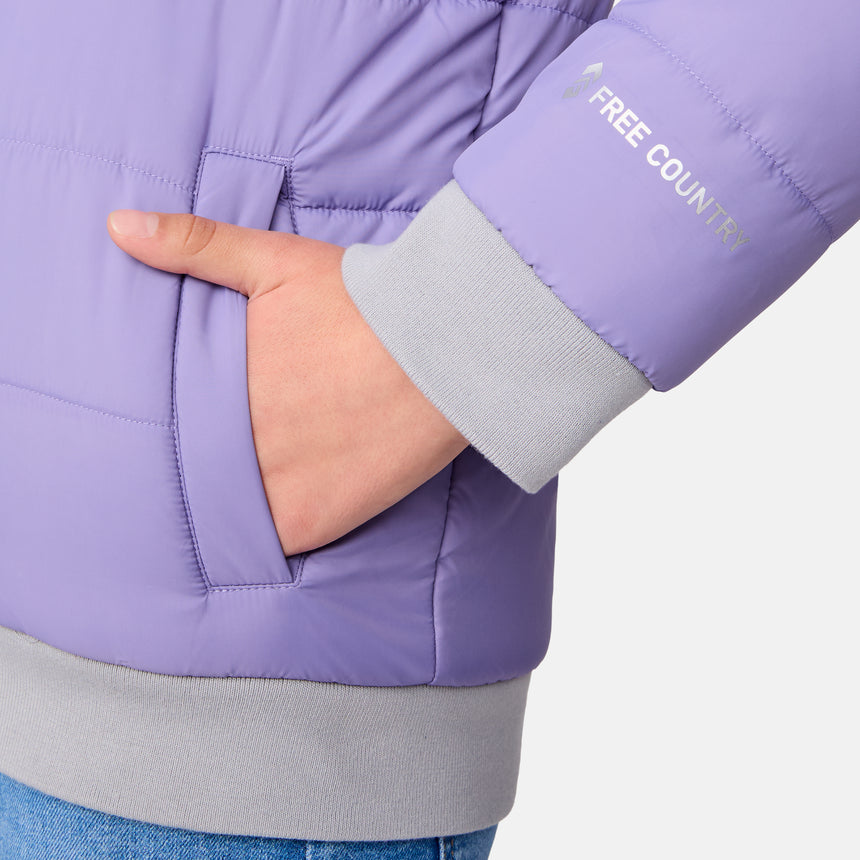 A person wearing the Clearance Girls' Poofie Reversible Puffer Jacket in light purple recycled polyester, with a hand in the pocket. The jacket sleeve features "FREE COUNTRY" text and gray cuffs, and blue jeans are partially visible.