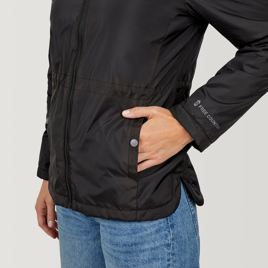 Woman wearing Free Country Women's Cascade Windshear Jacket in black with a full front zipper opening, soft lining, and water resistant and wind resistant recycled polyester stretch performance fabric, light grey background. Best women’s jacket for windy weather.
