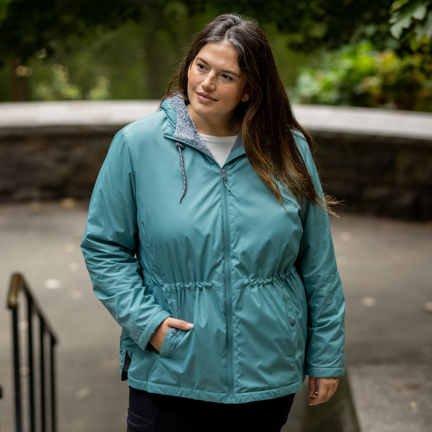 Woman wearing Free Country Women's Cascade Windshear Jacket in light blue with a full front zipper opening, soft lining, and water resistant and wind resistant recycled polyester stretch performance fabric. Best women’s jacket for windy weather.