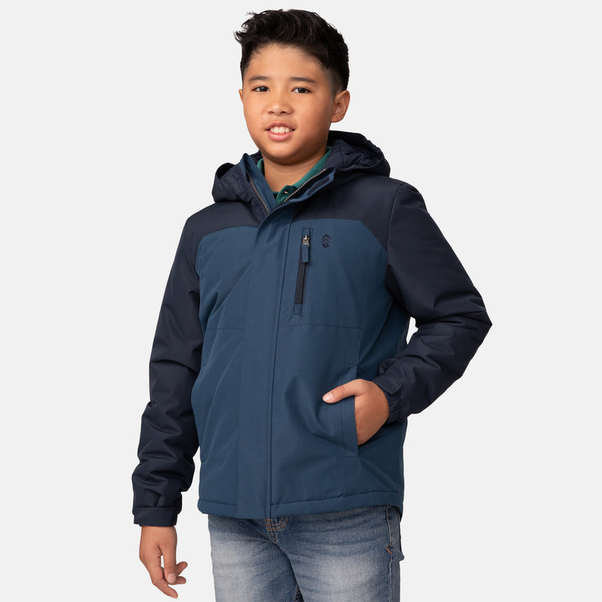 A boy wearing the Clearance Boys' Mount Avon Midweight Jacket in Ocean and jeans stands with one hand in his pocket, smiling at the camera against a plain white background.