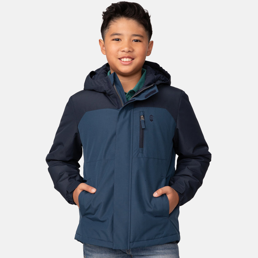 A smiling boy wearing the Clearance Boys' Mount Avon Midweight Jacket, featuring a blue water-resistant design with his hands in the pockets, stands against a plain light gray background.