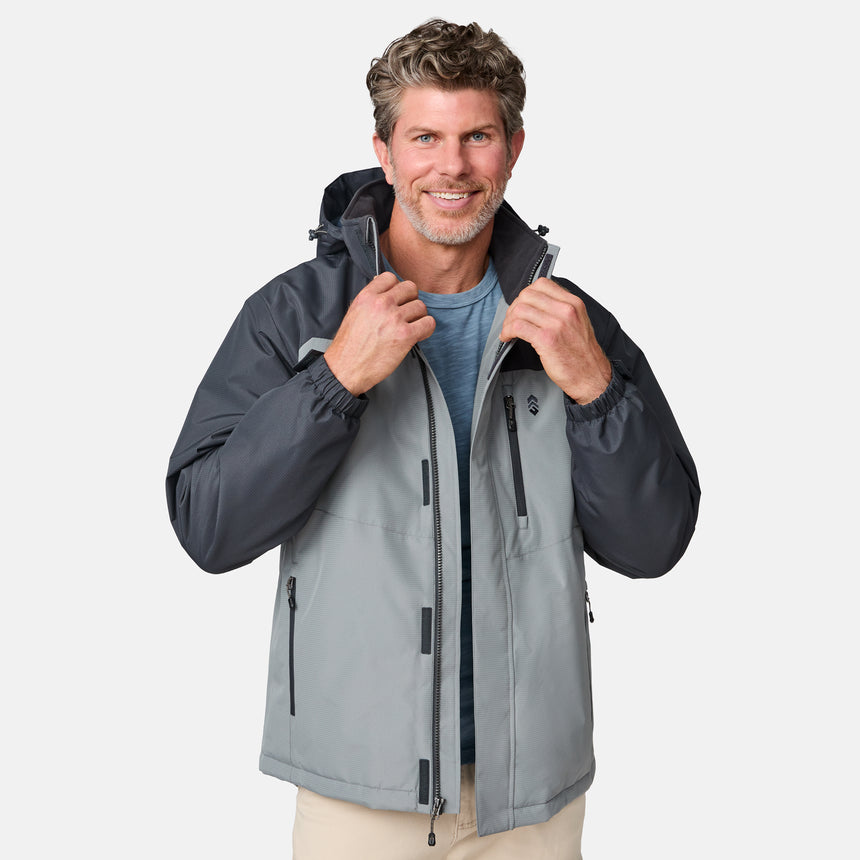 A man with wavy hair smiles while wearing the Clearance Men's Arvon Insulated Jacket in two-tone gray over a blue shirt, holding its zipper and standing against a plain white background.