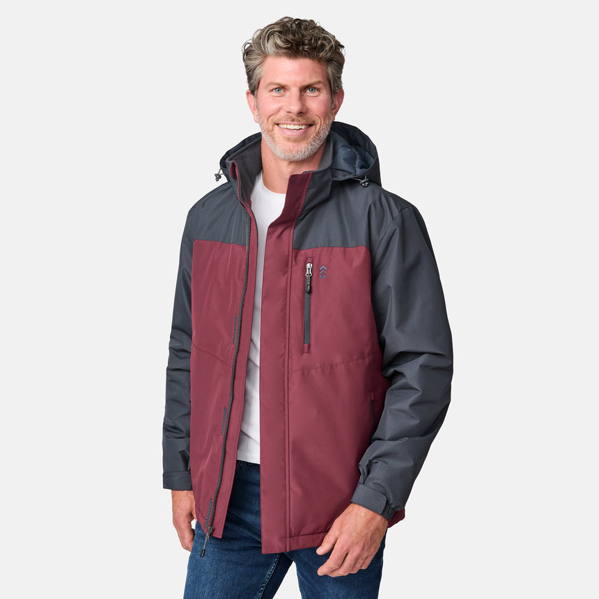 A man with short, wavy gray hair and a beard smiles in a maroon and dark gray Clearance Men's Arvon Insulated Jacket over a white shirt and blue jeans, standing against a plain light background.