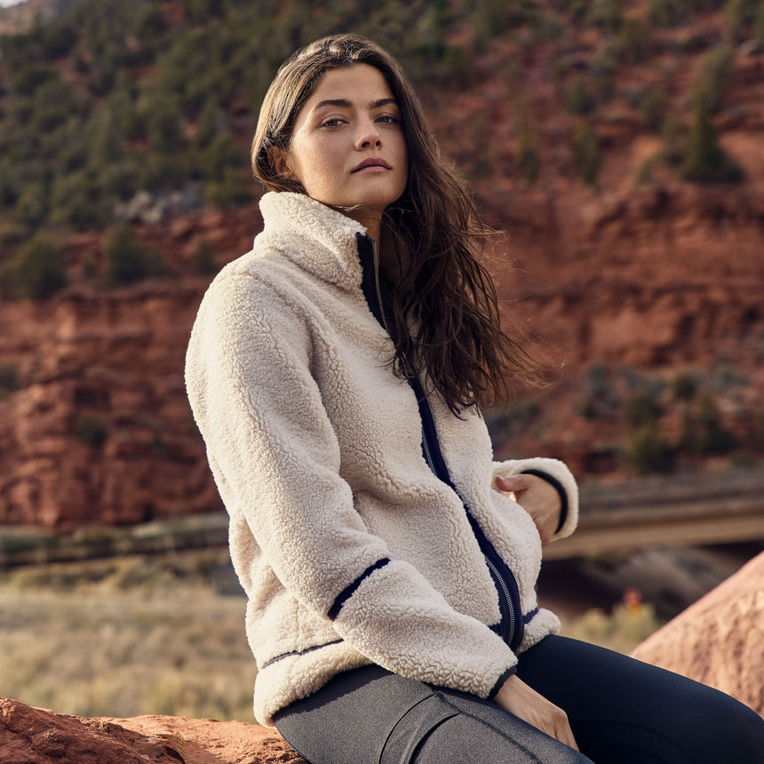 A woman wearing a cream colored shearling jacket with a blurred desert background