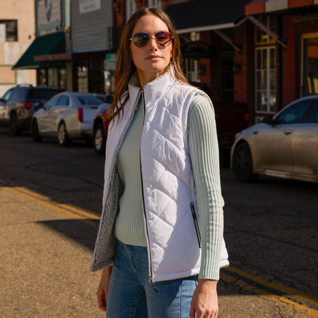 Woman wearing Free Country Women's Expedition Stratus Lite Reversible Vest in light grey with a full front zipper opening, soft lining, recycled polyester filling, and water resistant and wind resistant performance fabric. Best women’s vest for chilly weather.