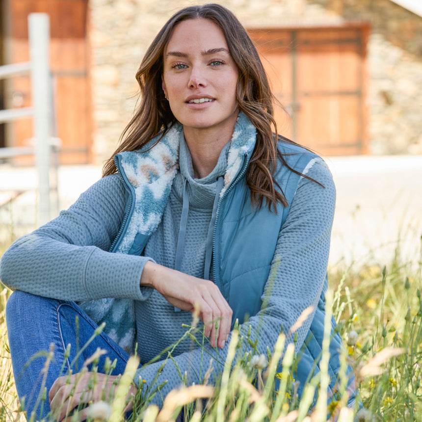 Woman wearing the Free Country Women's Venture Stratus Lite Reversible Vest in light blue, featuring a geometric-print Butter Pile® lining and horizontal quilted overlay