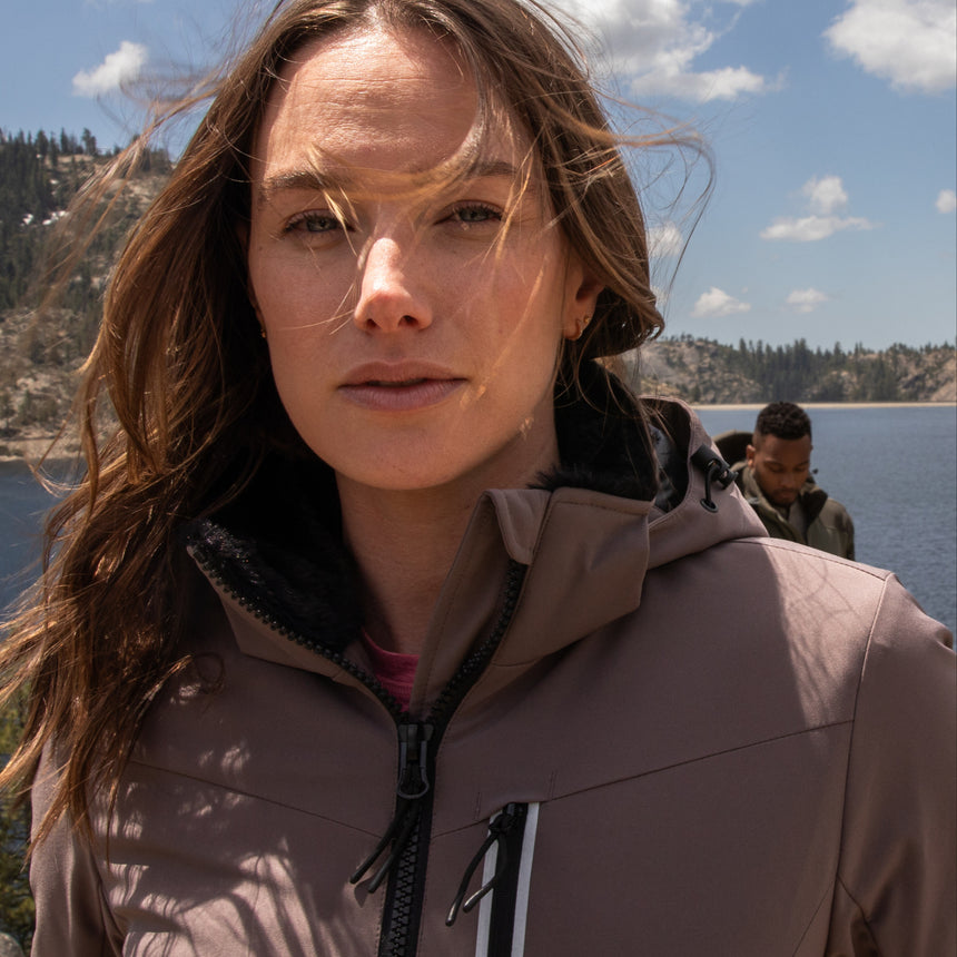 Woman wearing Free Country Women's FreeCycle® Thermo Super Softshell® II Jacket in light brown with a full front zipper opening, lower pockets, soft lining, a detachable hood with an adjustable drawcord, and water resistant and wind resistant stretch performance fabric. Best women’s jacket for winter weather.
