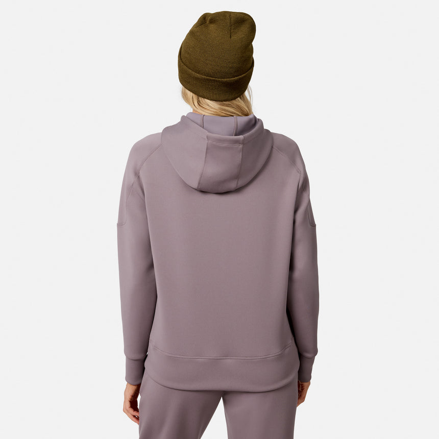 A woman is seen from the back wearing a mauve Free Country Women’s Sueded Lush Pullover Hoodie with matching pants and a brown beanie, standing against a plain white background.
