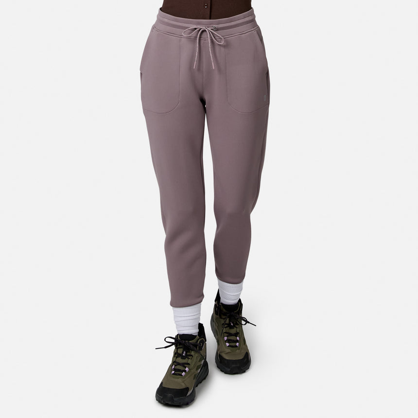 Model in Free Country Women’s Sueded Lush Jogger (mauve, 4-way stretch, front pockets, drawstring waist), white socks, and green hiking shoes on white background. Upper body not visible.