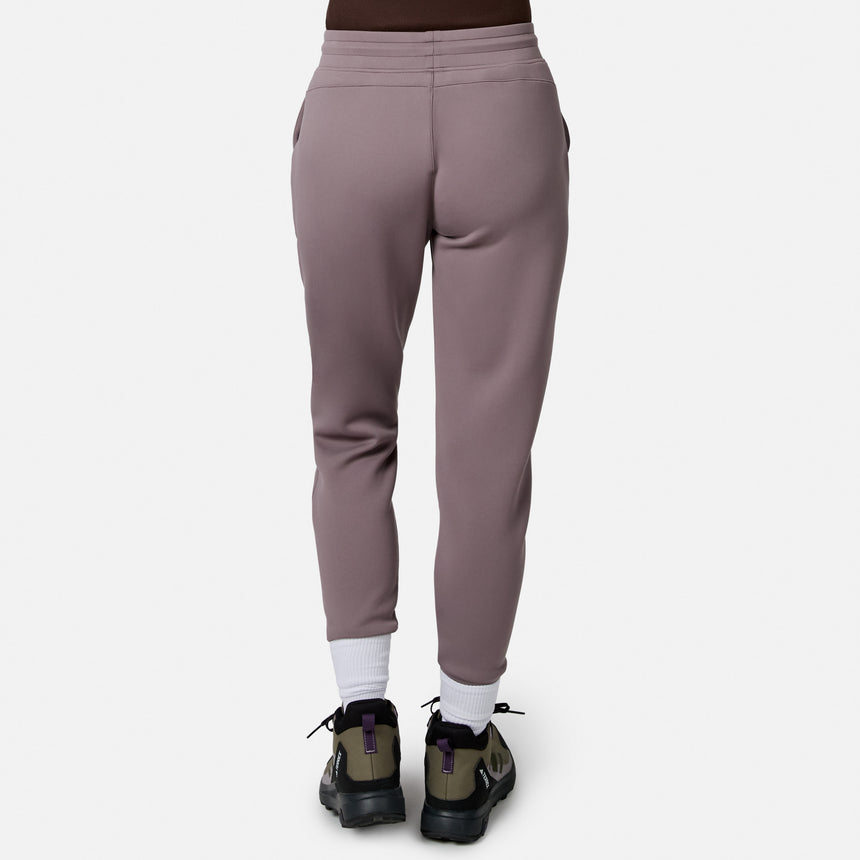 Person facing away, wearing Free Country Women’s Sueded Lush Jogger in mauve, white socks, and green-black sneakers with purple accents, standing against a plain white background.