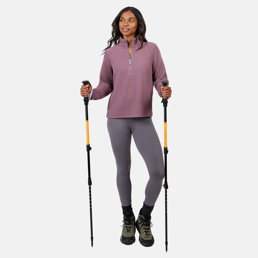 A woman stands with hiking poles, wearing the Free Country Women’s Ripple Knit Half Zip Top in mauve, gray leggings, black socks, and green hiking boots—breathable and perfect for casual layering on any outdoor adventure.