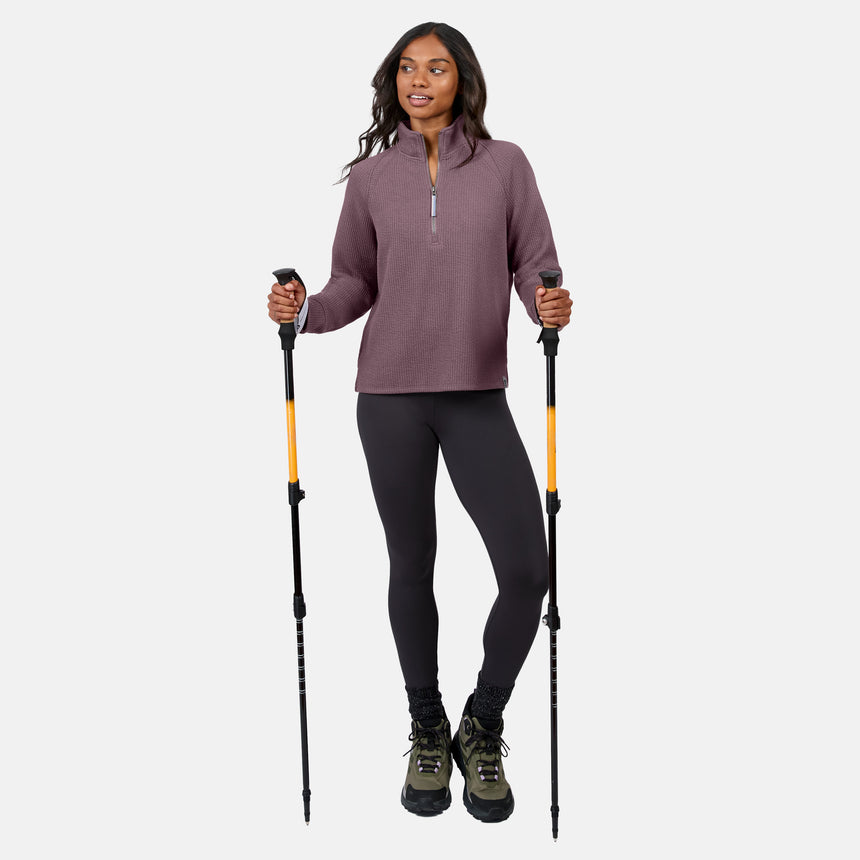 A woman stands with hiking poles, wearing the Free Country Women’s Ripple Knit Half Zip Top in mauve, gray leggings, black socks, and green hiking boots—breathable and perfect for casual layering on any outdoor adventure.