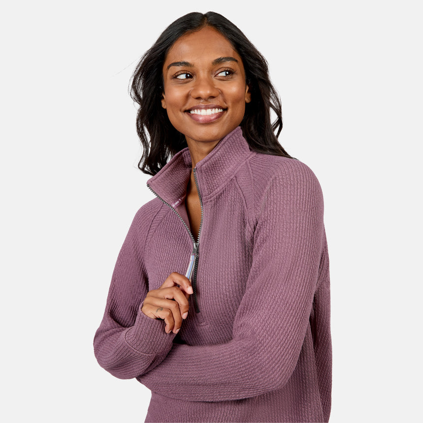 A woman with long dark hair smiles and looks to the side while wearing the Free Country Women’s Ripple Knit Half Zip Top, perfect for casual layering, against a plain light background.