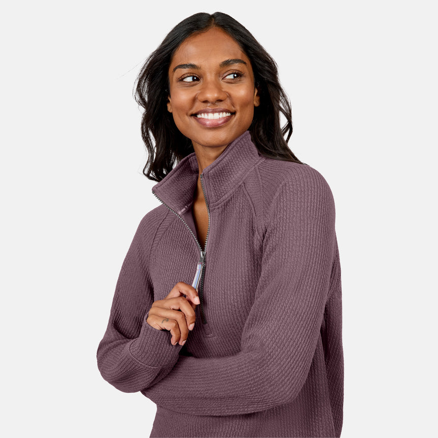 A woman with long dark hair smiles and looks to the side while wearing the Free Country Women’s Ripple Knit Half Zip Top, perfect for casual layering, against a plain light background.