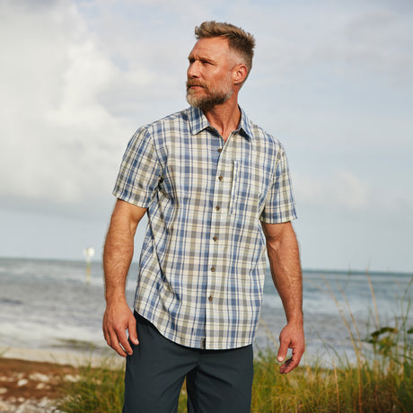 Man is wearing Free Country Men's Excursion Short Sleeve Poplin Shirt in Dusty Vine Plaid, size M, made from lightweight moisture wicking polyester fabric featuring vent at the back, full button down front, and a stand collar, styled with navy shorts #color_dusty-vine-plaid