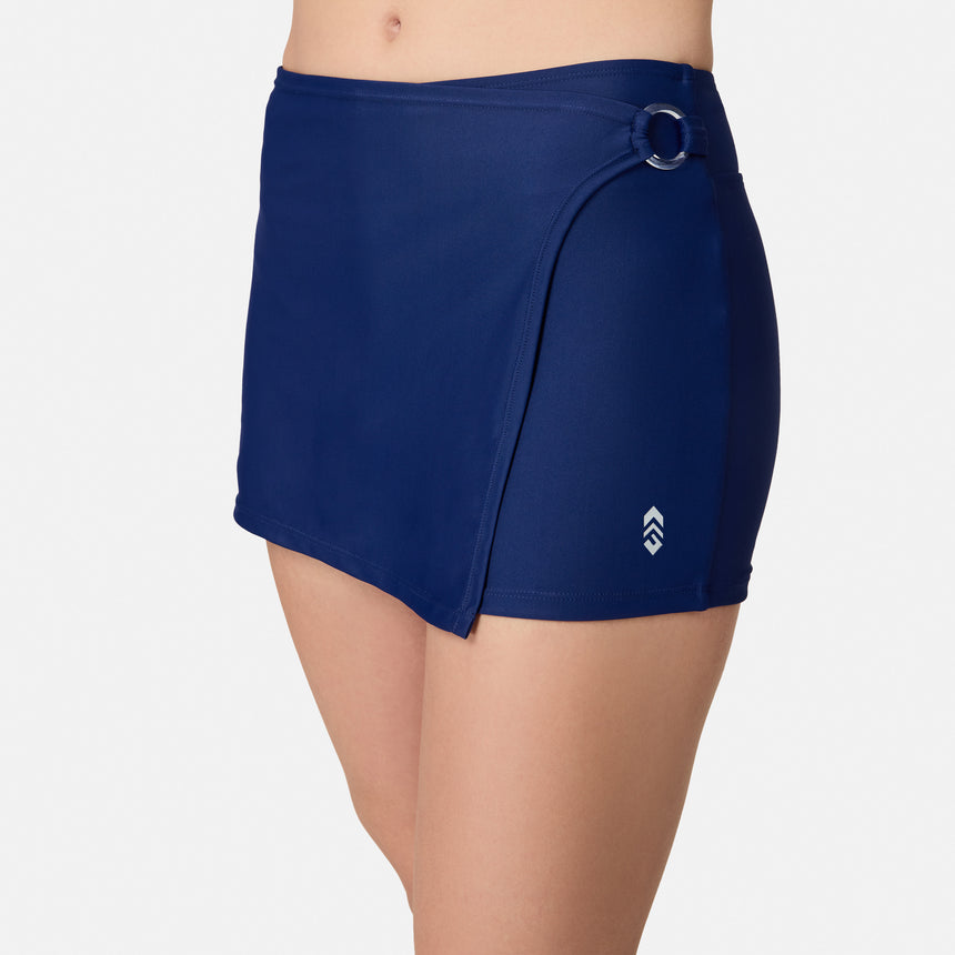 A person wears the Free Country Women's Fully Lined Swim Skort in navy, featuring a side ring detail and small white logo near the hem, photographed from waist to mid-thigh against a plain white background.