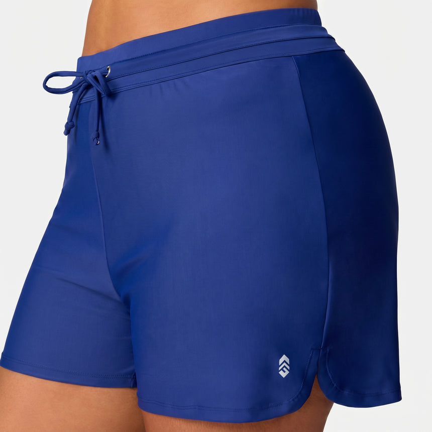 Close-up of a person wearing Free Country Women's Plus Size Drawstring Swim Short in royal blue, featuring a drawstring waistband, small white logo near the hem, and quick-dry comfort for active days by the water.