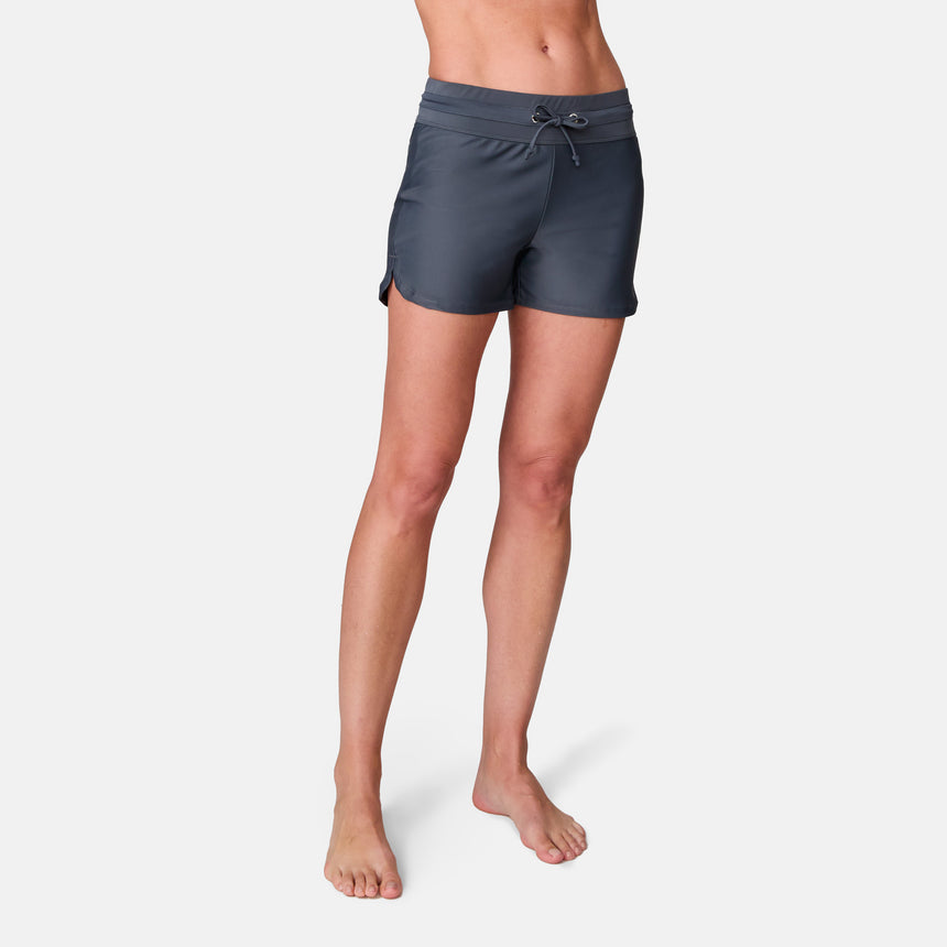 A person models the Free Country Women's Drawstring Swim Short in dark gray, standing barefoot against a plain white background, shown from the waist down.