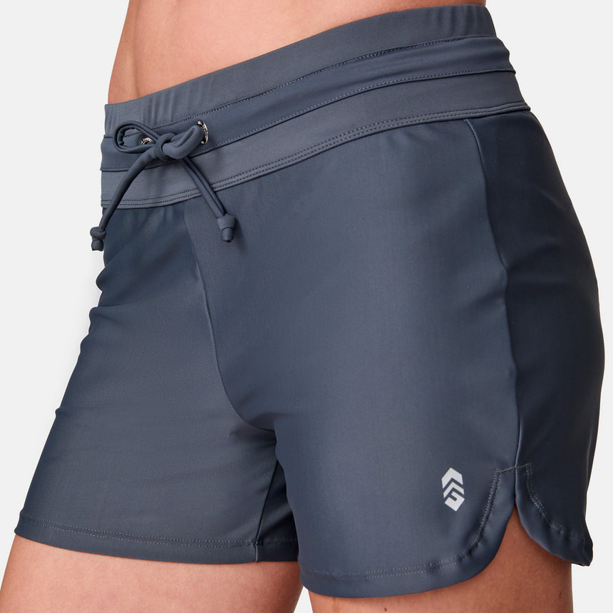 Close-up of a person wearing Free Country Women's Drawstring Swim Short in dark gray, featuring a drawstring waist and a small white logo near the left hem.