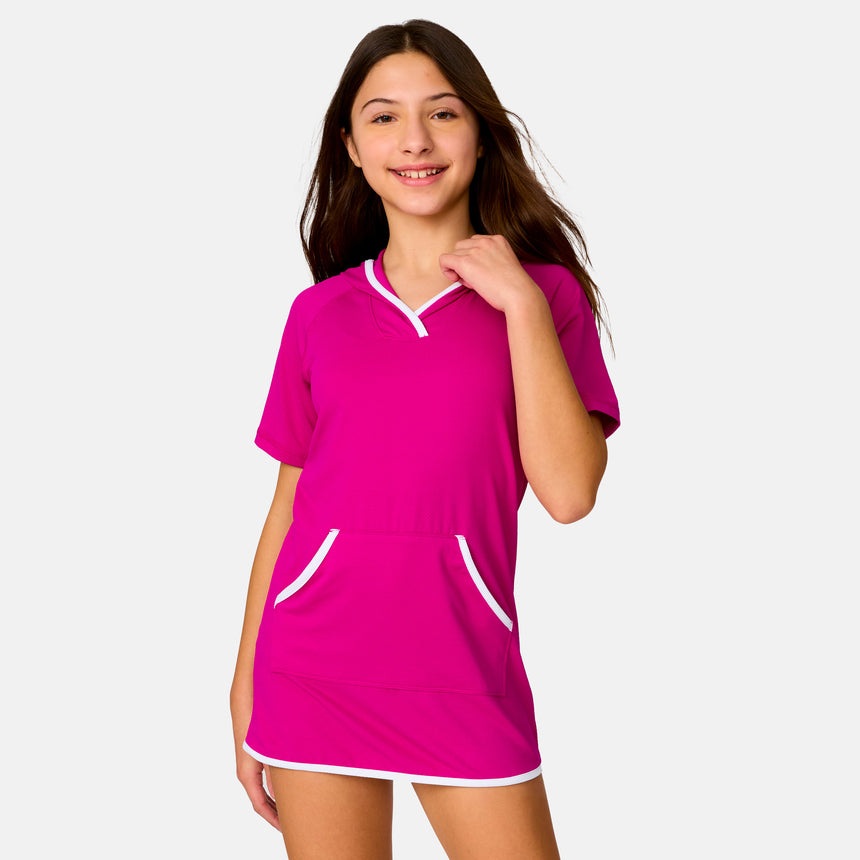 A smiling young person with long brown hair wears the Clearance Girls' SunFree UPF Dress in bright pink with white trim, offering sun protection as she stands against a plain light background.