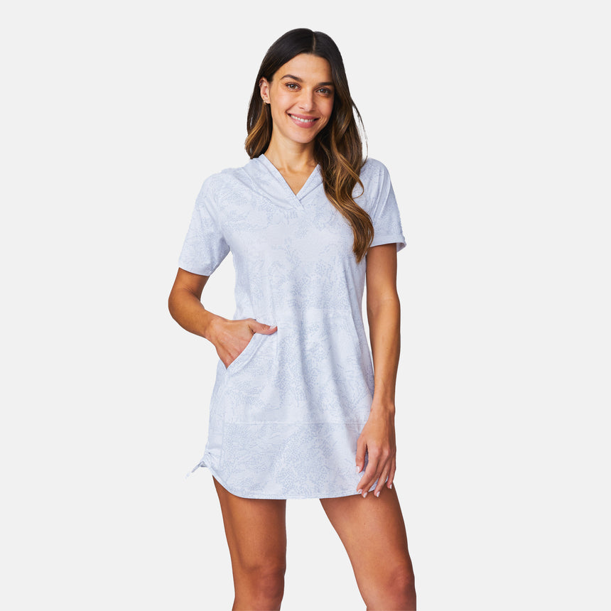 A woman smiles in the Free Country Women's SunFree UPF Dress, a light blue short-sleeve hoodie cover-up with a front pocket, made from recycled polyester. She poses against a white background, highlighting this eco-friendly dress.