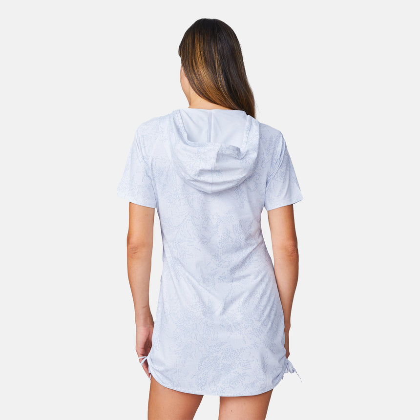 A woman stands facing away, wearing the Free Country Women's SunFree UPF Dress—a light-colored, short-sleeve hooded dress with subtle patterns and UPF 50+ sun protection—set against a plain white background.