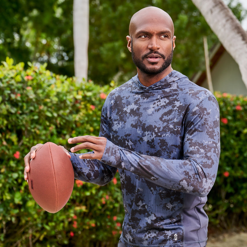 Man wearing Free Country Men's SunFree UPF Printed Hoodie in Charcoal Camo, size M throwing a football at the park, made from anti-odor, breathable lightweight recycled polyester performance fabric featuring a classic active fit #color_charcoal-camo
