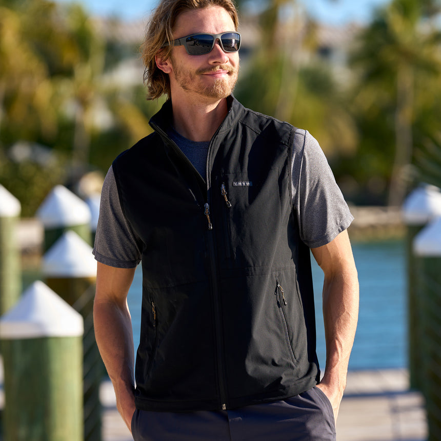 Man wearing Free Country Men's Stretch Rip Stop Adventure Vest in Dark Black, size M, made from wind resistant lightweight stretch polyester performance fabric featuring a convertible collar and full front zip closure #color_black