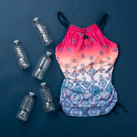 A colorful one-piece swimsuit with pink and blue patterns is laid flat on a dark blue background, surrounded by five empty plastic bottles.