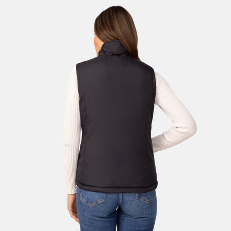A woman with straight brown hair stands with her back to the camera, wearing Clearance's Women's Cascade Canvas 3-in-1 Systems Jacket over a white ribbed top and blue jeans, in front of a plain light background.