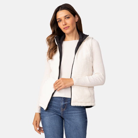 A woman wears the Women's Cascade Canvas 3-in-1 Systems Jacket by Clearance, featuring a white sherpa jacket with a removable reversible inner vest over a light ribbed sweater and blue jeans, standing against a plain light background.