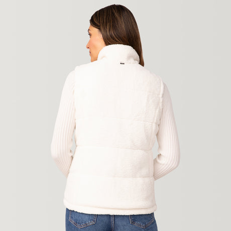A woman with brown hair is seen from the back, wearing the Clearance Women's Cascade Canvas 3-in-1 Systems Jacket over a white ribbed long-sleeve top and blue jeans, standing against a neutral background.