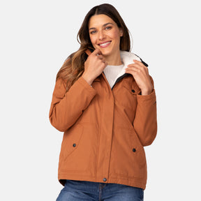 A smiling woman with long brown hair wears the Clearance Women's Cascade Canvas 3-in-1 Systems Jacket over a white sweater and blue jeans, standing against a plain light background.