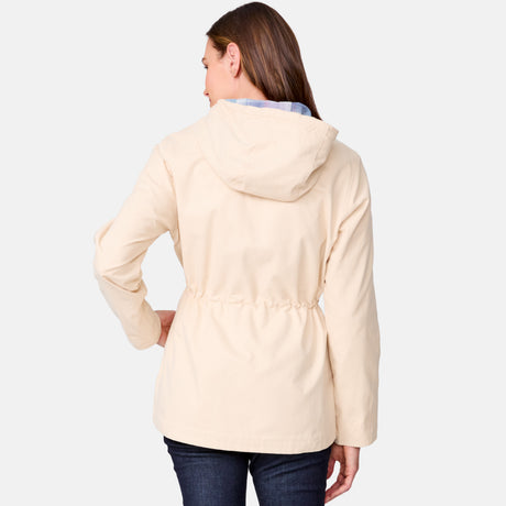 A woman with long brown hair, seen from the back, is wearing the Clearance Women’s Lightweight Cascade Canvas Jacket in light beige with a hood and dark jeans against a plain light background.