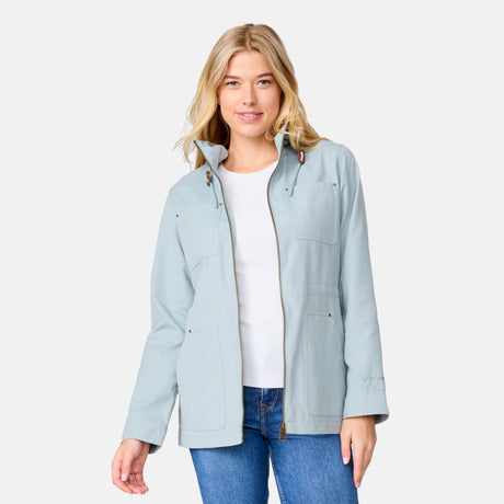 A woman with blonde hair models the Clearance Women's Lightweight Cascade Canvas Jacket in light blue over a white shirt and blue jeans, standing against a light gray background and smiling at the camera.