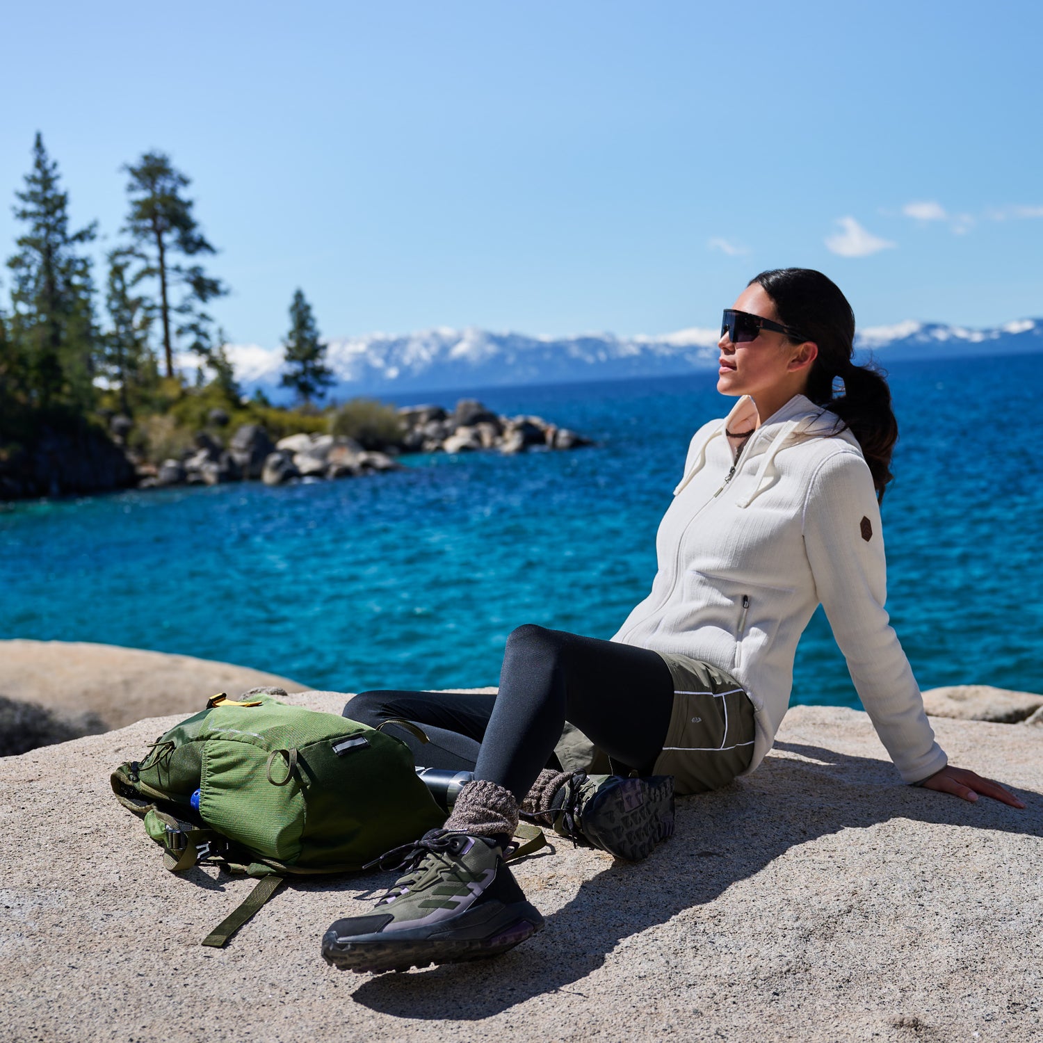 Woman relaxing on lakeside rocks in a white Free Country fleece jacket