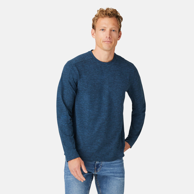 A man with short, curly blond hair wears a Free Country Men's FreeCycle® Sueded Spacedye Long Sleeve Crew Neck in Deep Navy and light blue jeans, standing against a plain white background.
