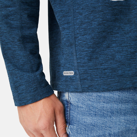 A close-up of a person in the Free Country Men's FreeCycle® Sueded Spacedye Long Sleeve Crew Neck, blue heathered, with a MICRO-TECH label near the hem, styled with light blue jeans and their hand relaxed at their side.