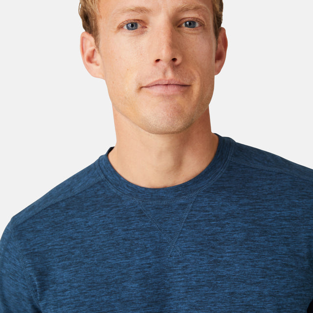 A man wears the Free Country Men's FreeCycle® Sueded Spacedye Long Sleeve Crew Neck, made with eco-friendly fabric, while looking at the camera. Only his face and upper torso are shown against a plain white background.