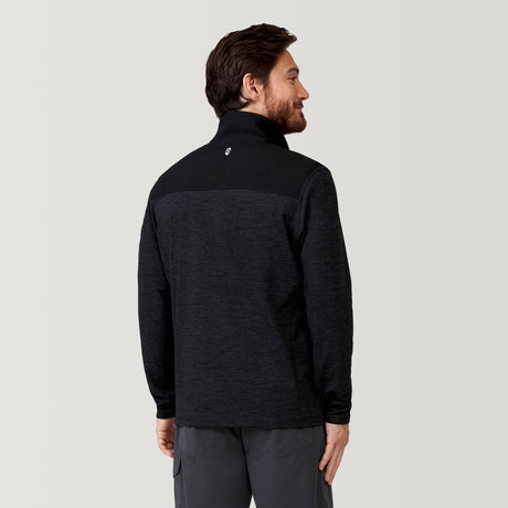A man with short brown hair and a beard faces away, wearing the Clearance Men's Sueded Spacedye 1/2 Zip Colorblock Mock Neck Shirt and dark pants, against a plain light gray background.