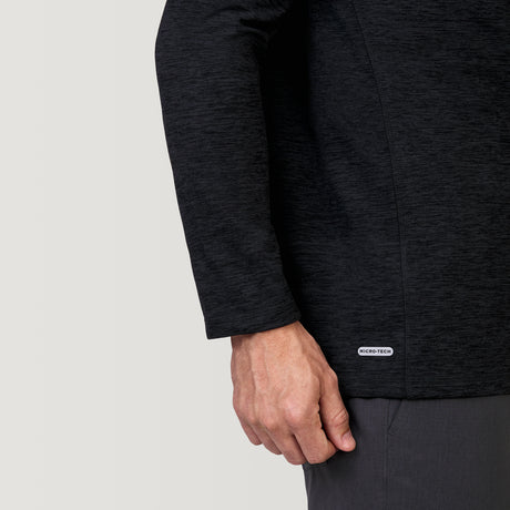 A close-up shows a person wearing the Clearance Men's Sueded Spacedye 1/2 Zip Colorblock Mock Neck Shirt in dark gray, paired with gray pants. Their left arm rests by their side and a small GEO-TECH label appears near the shirt’s hem.