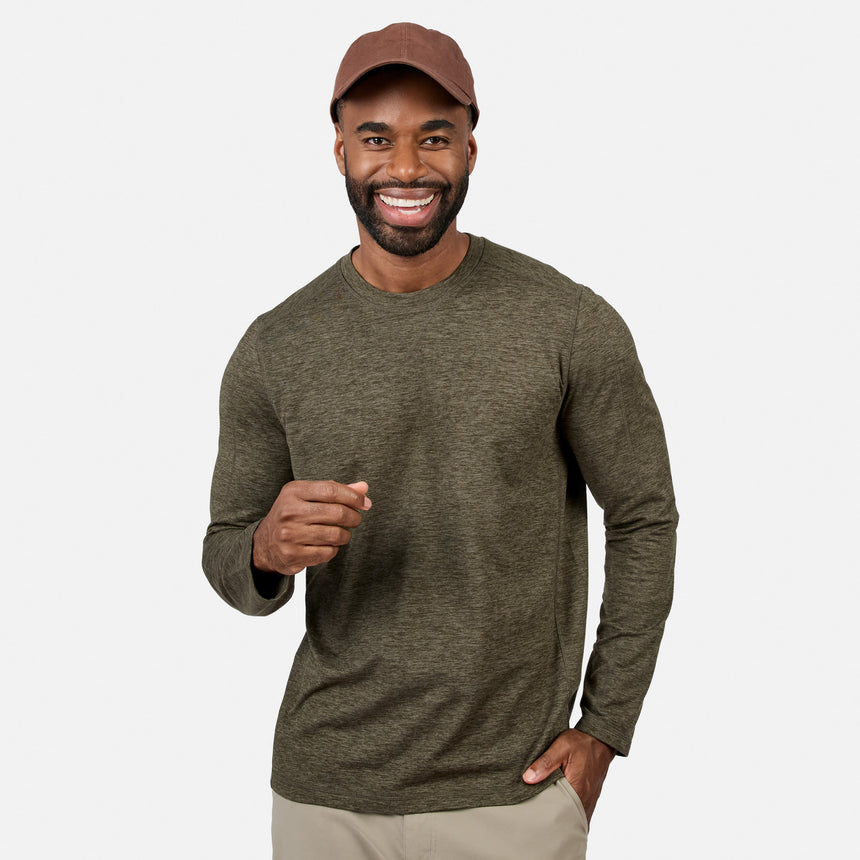 [Model is wearing size M.] A smiling man wearing a heathered olive green long-sleeve crewneck shirt, a brown baseball cap, and khaki pants, standing against a light gray studio background.