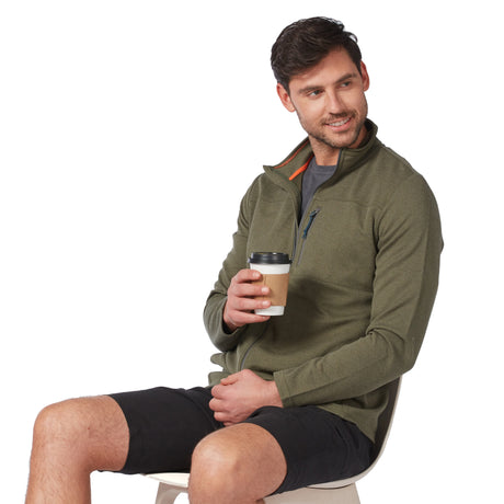 A man wearing an olive green Men’s FreeCycle® Double Knit Full Zip Fleece Jacket and black shorts sits on a chair while holding a disposable coffee cup.
